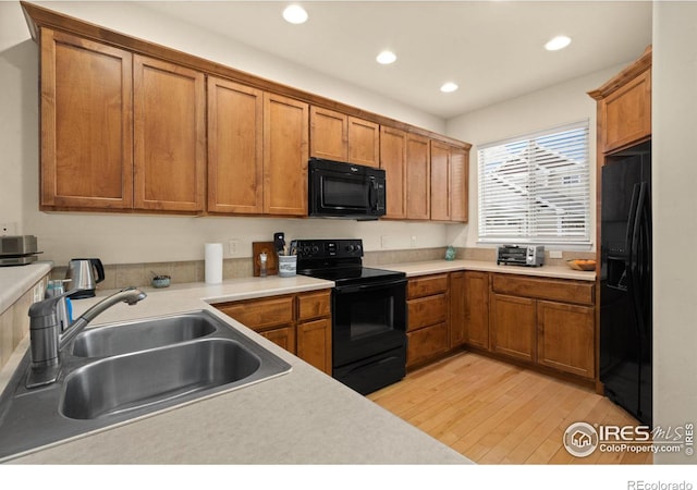 kitchen with black appliances, brown cabinetry, light wood-type flooring, and a sink