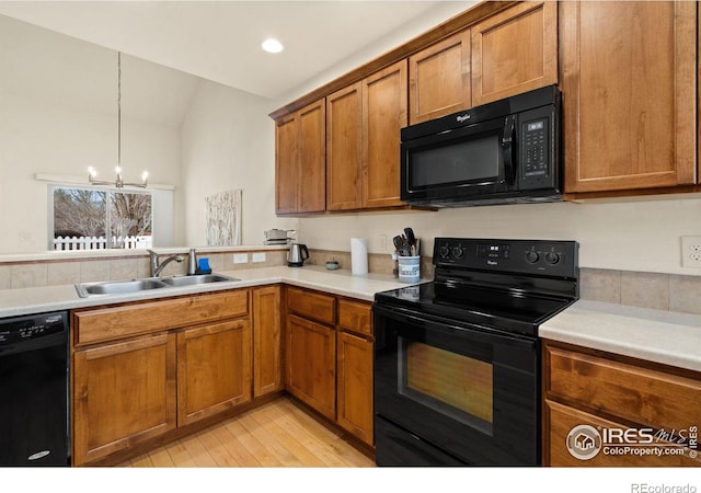 kitchen with brown cabinets, black appliances, a sink, an inviting chandelier, and light countertops