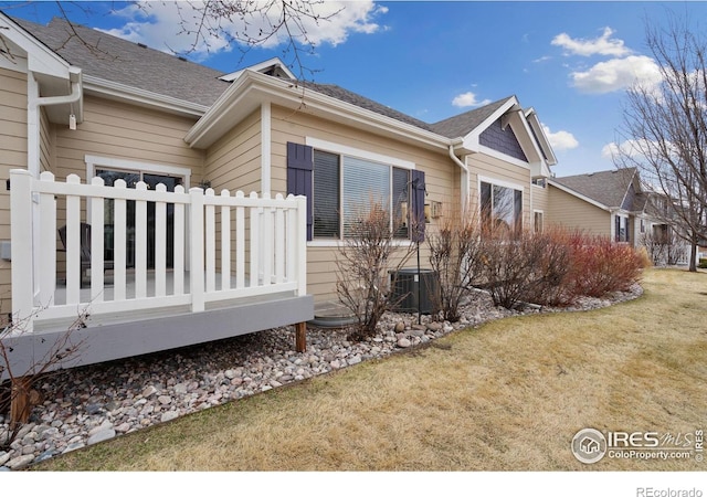 view of side of property with central AC unit, a lawn, a wooden deck, and roof with shingles