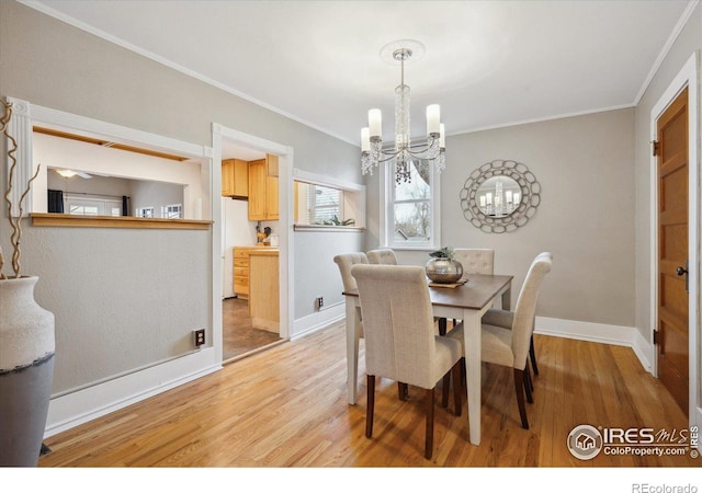 dining space featuring light wood finished floors, a notable chandelier, crown molding, and baseboards