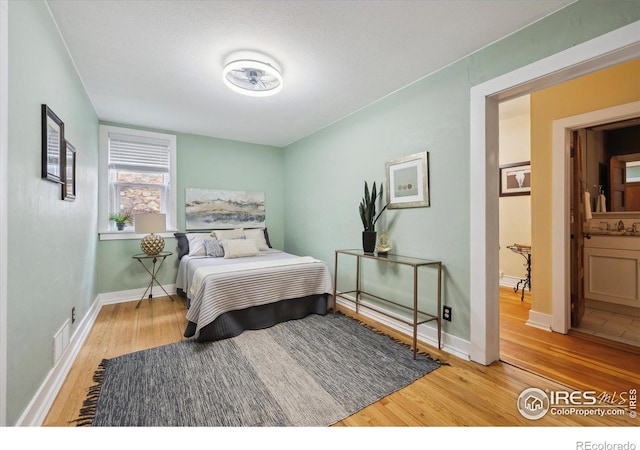 bedroom with visible vents, a sink, baseboards, and wood finished floors