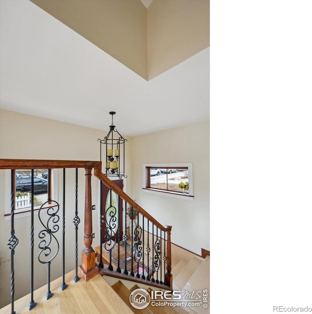 staircase with a healthy amount of sunlight, wood finished floors, and an inviting chandelier