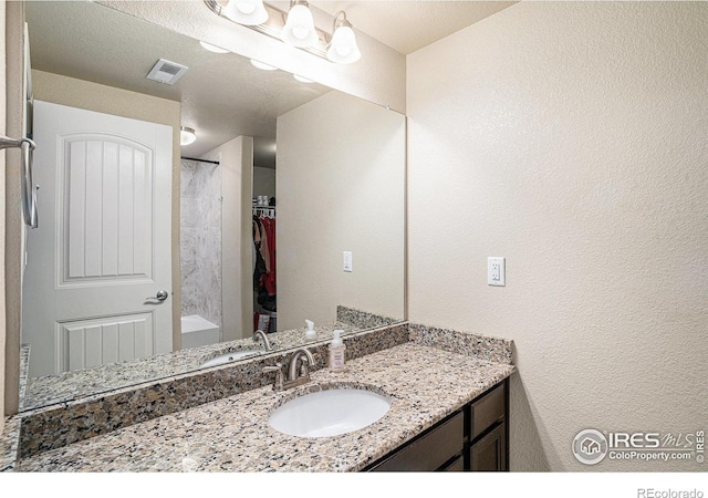 bathroom with vanity, a textured wall, visible vents, and walk in shower