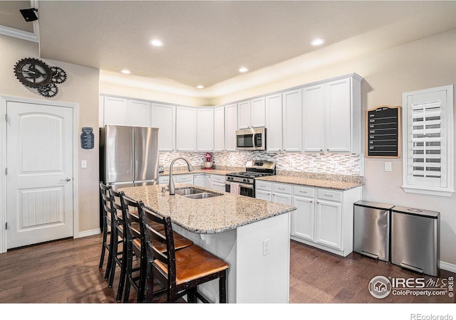 kitchen featuring dark wood-style floors, a sink, stainless steel appliances, a kitchen breakfast bar, and tasteful backsplash