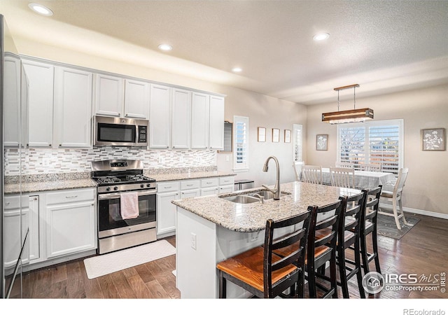 kitchen featuring light stone counters, dark wood-style floors, a sink, decorative backsplash, and appliances with stainless steel finishes