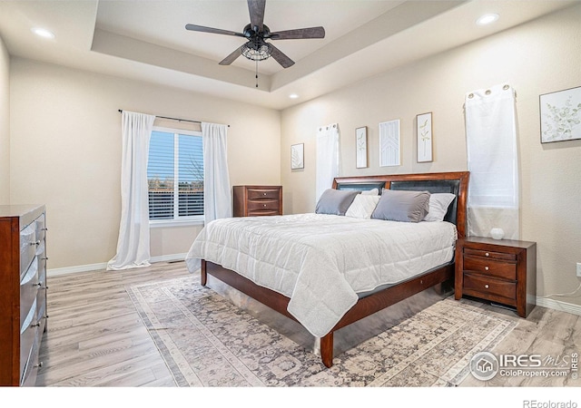 bedroom featuring a raised ceiling, light wood-style flooring, recessed lighting, and baseboards