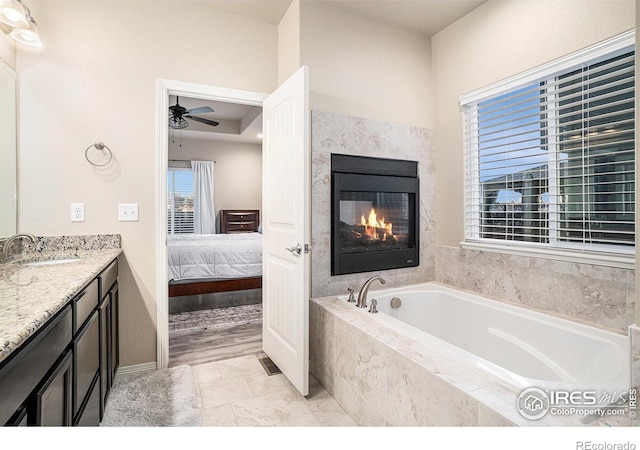 full bathroom with vanity, a ceiling fan, a glass covered fireplace, a bath, and connected bathroom