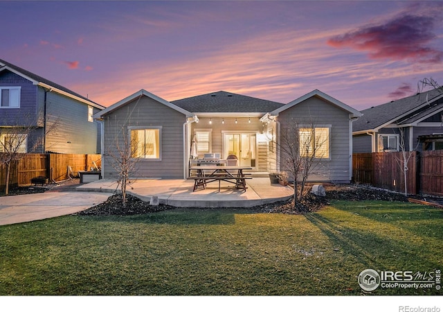 back of property at dusk featuring a patio area, a yard, and a fenced backyard