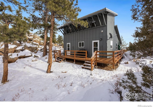 snow covered house with a wooden deck and board and batten siding