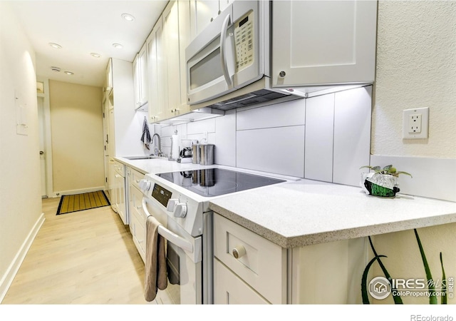 kitchen featuring baseboards, recessed lighting, light wood-style flooring, white appliances, and a sink