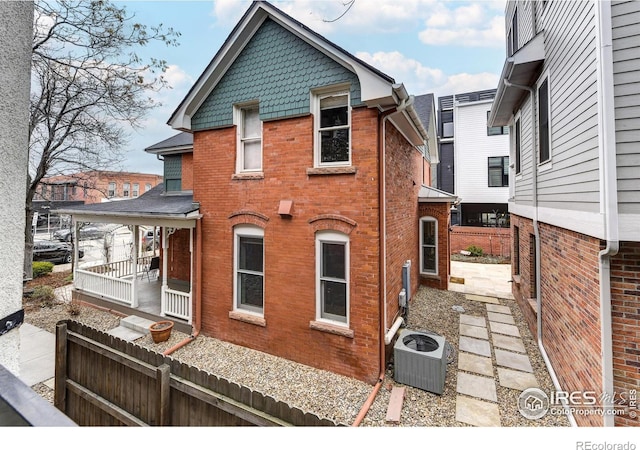 view of property exterior featuring brick siding, central AC unit, and fence