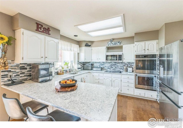 kitchen featuring a peninsula, a sink, stainless steel appliances, light countertops, and white cabinetry