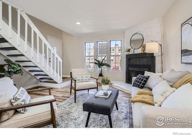 living room featuring wood finished floors, baseboards, recessed lighting, a fireplace, and stairs