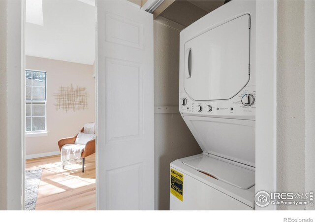 clothes washing area featuring stacked washer / drying machine, wood finished floors, and laundry area