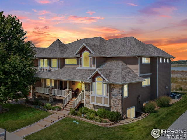 view of front of property with a shingled roof, stairway, a porch, a lawn, and stone siding