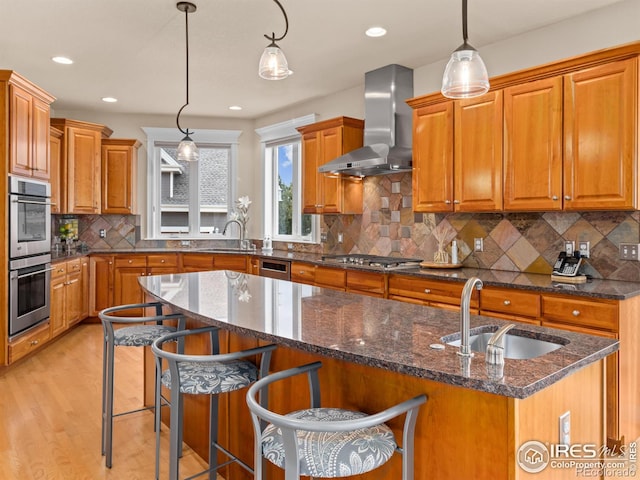 kitchen featuring wall chimney exhaust hood, brown cabinets, appliances with stainless steel finishes, and a sink