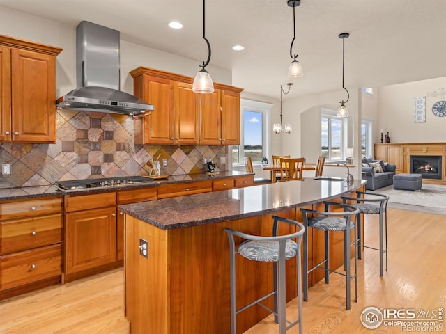 kitchen featuring a kitchen island, wall chimney range hood, a breakfast bar, light wood-style flooring, and stainless steel gas stovetop