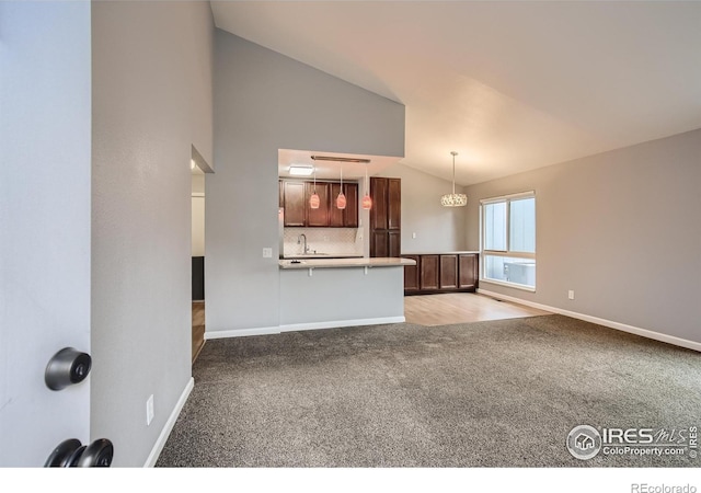 unfurnished living room featuring light colored carpet, baseboards, lofted ceiling, and a sink