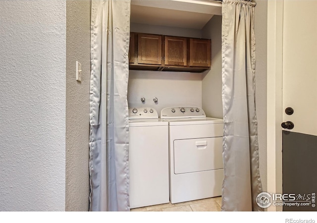 laundry room featuring washer and clothes dryer, light tile patterned floors, cabinet space, and a textured wall