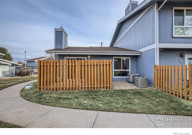 back of property with fence, roof with shingles, cooling unit, a chimney, and a yard