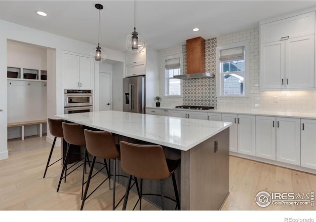 kitchen with a breakfast bar, appliances with stainless steel finishes, a kitchen island, and wall chimney range hood