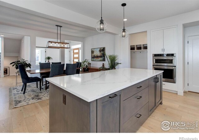 kitchen with light stone counters, a kitchen island, stainless steel double oven, light wood-style floors, and decorative light fixtures