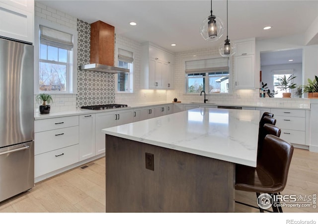 kitchen with a kitchen bar, a sink, white cabinetry, stainless steel appliances, and wall chimney exhaust hood