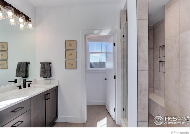 bathroom with vanity, baseboards, tile patterned flooring, and tiled shower