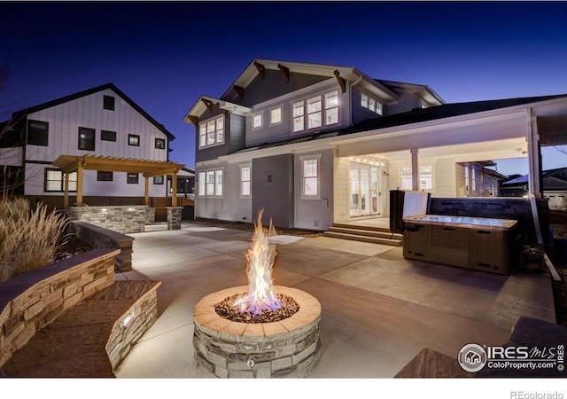 patio at night featuring a fire pit and a hot tub