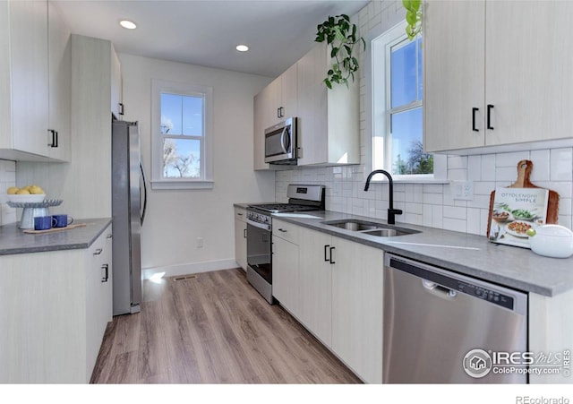 kitchen with baseboards, light wood-style flooring, a sink, decorative backsplash, and appliances with stainless steel finishes