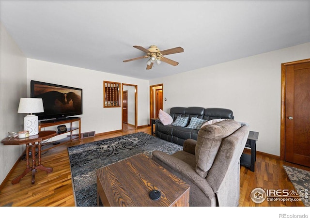 living area featuring baseboards, wood finished floors, visible vents, and ceiling fan