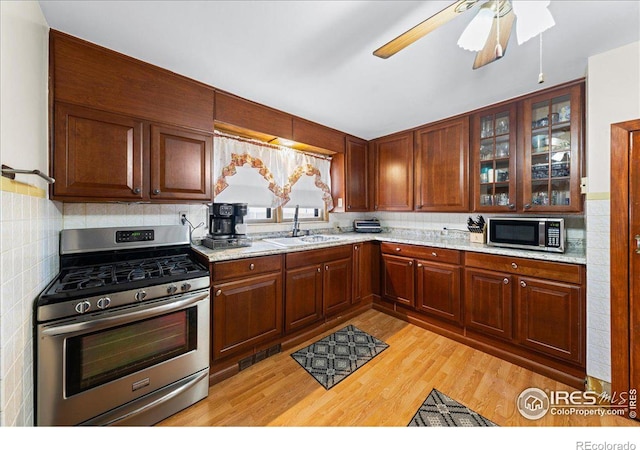 kitchen with light wood-type flooring, visible vents, a sink, appliances with stainless steel finishes, and glass insert cabinets