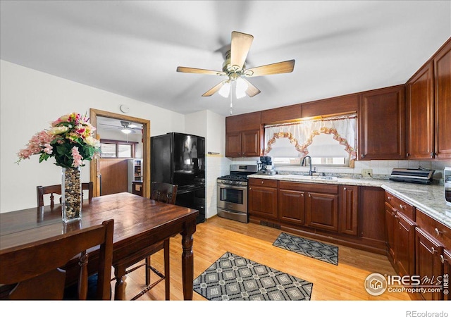 kitchen featuring light wood-type flooring, stainless steel gas stove, a sink, freestanding refrigerator, and ceiling fan