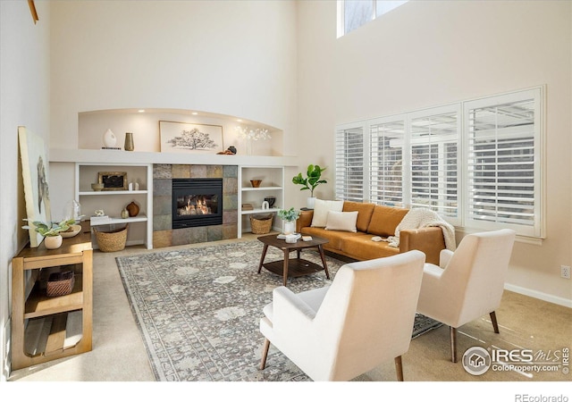 carpeted living area with built in features, baseboards, a towering ceiling, and a tile fireplace