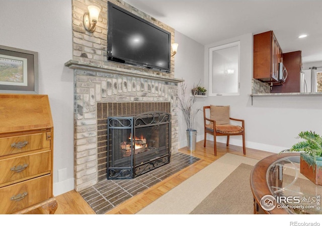 living area with recessed lighting, baseboards, a brick fireplace, and wood finished floors