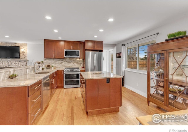 kitchen featuring a sink, backsplash, stainless steel appliances, light wood finished floors, and light stone countertops