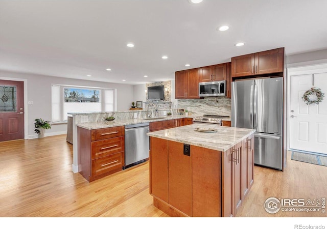 kitchen with light stone counters, a peninsula, light wood-style floors, stainless steel appliances, and a sink