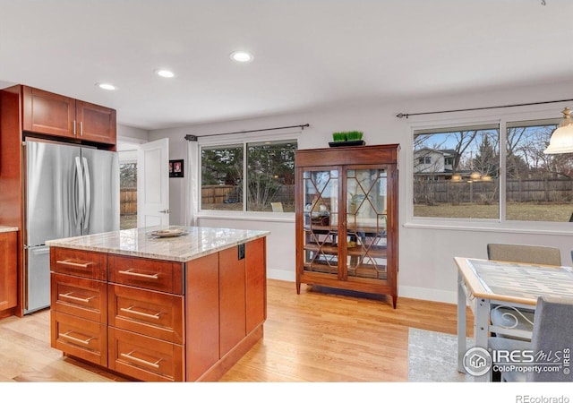 kitchen with a wealth of natural light, light wood finished floors, light stone countertops, and freestanding refrigerator