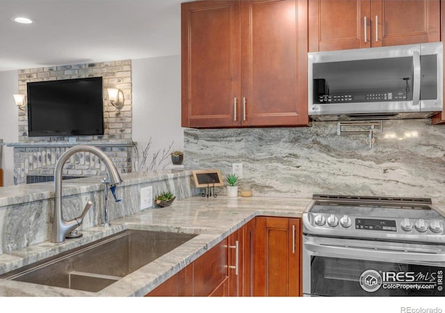 kitchen with light stone counters, a sink, appliances with stainless steel finishes, brown cabinets, and backsplash