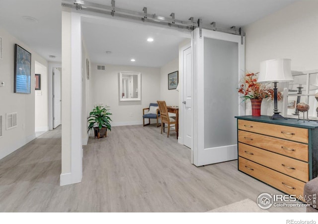 living area with a barn door, light wood-style floors, visible vents, and baseboards