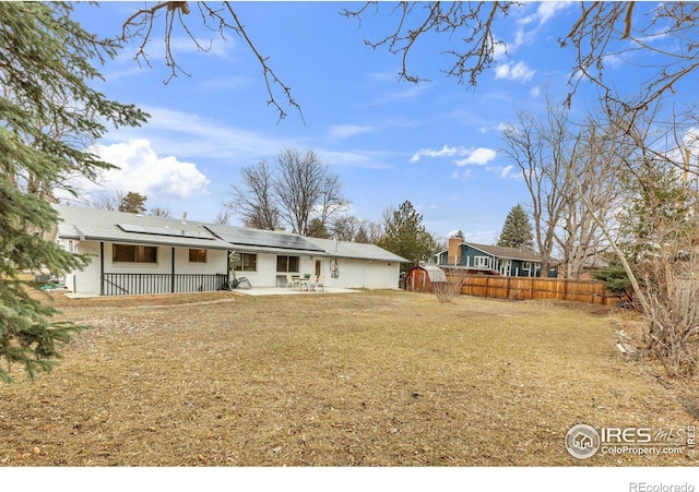 back of property featuring a patio area, roof mounted solar panels, a lawn, and fence