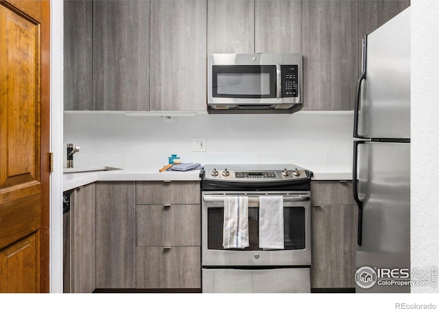 kitchen featuring appliances with stainless steel finishes, modern cabinets, light countertops, and a sink