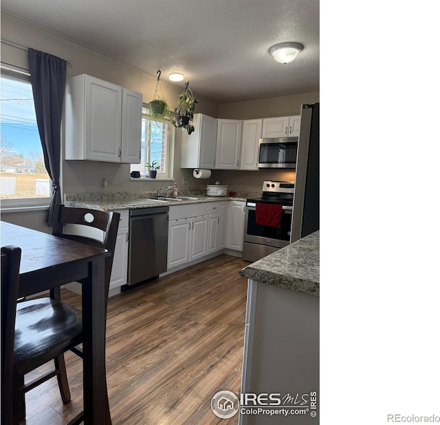 kitchen featuring dark wood-type flooring, appliances with stainless steel finishes, a textured ceiling, white cabinetry, and a sink