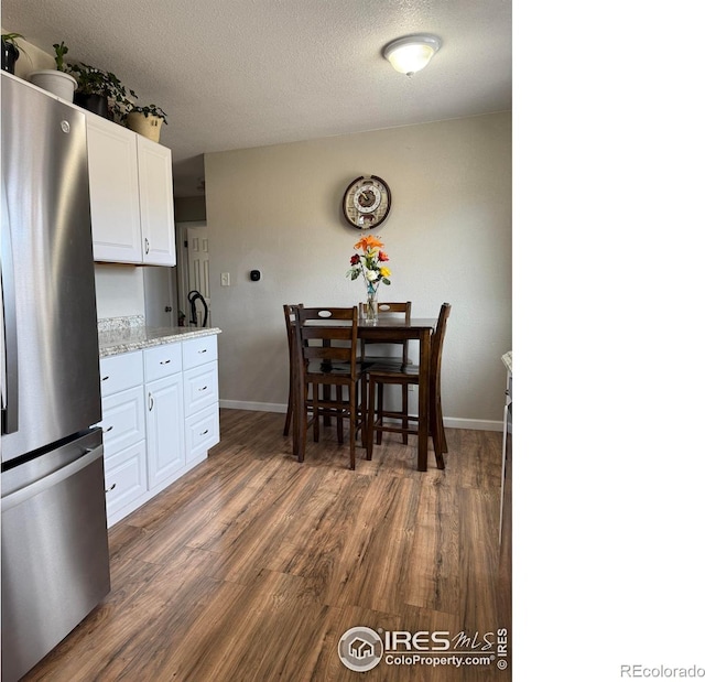 kitchen with light stone counters, dark wood-style floors, freestanding refrigerator, a textured ceiling, and white cabinetry