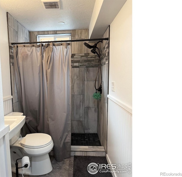 bathroom featuring visible vents, a wainscoted wall, toilet, tiled shower, and a textured ceiling