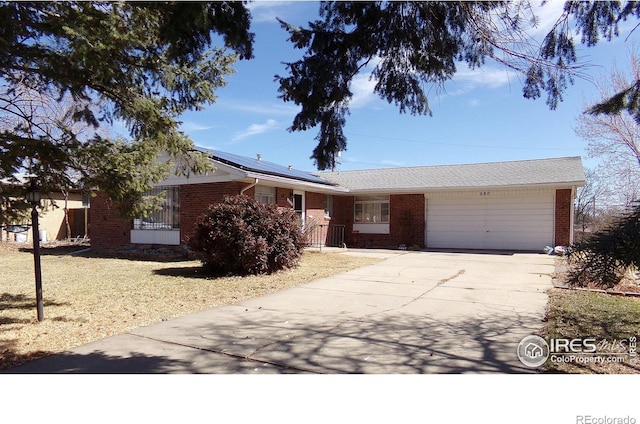 single story home featuring brick siding, roof mounted solar panels, an attached garage, and concrete driveway