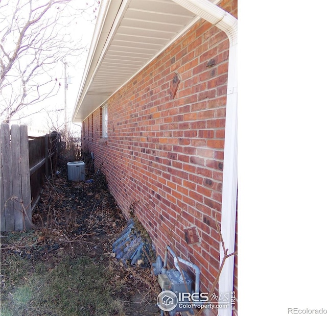 view of side of property with brick siding, central air condition unit, and fence