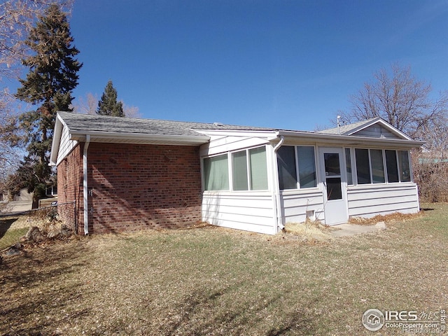 view of front of home with a front yard, brick siding, and a sunroom