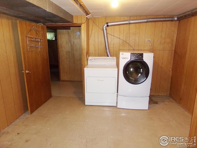 clothes washing area featuring laundry area, light floors, wooden walls, and separate washer and dryer