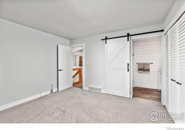 unfurnished bedroom with carpet flooring, visible vents, a textured ceiling, and a barn door